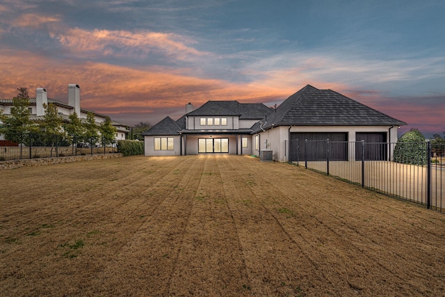 view of front of house with central AC unit, a garage, and a lawn