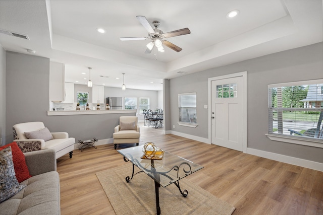 living room featuring ceiling fan, a raised ceiling, and light hardwood / wood-style flooring