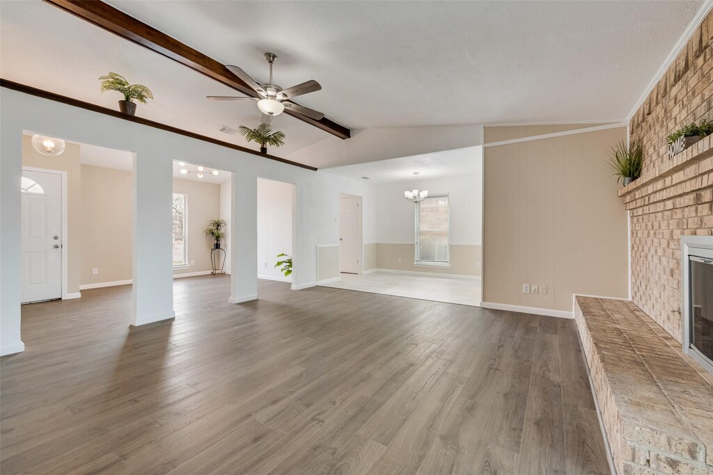 533 Doral Pl, Garland, TX 75043 - unfurnished living room featuring vaulted ceiling with beams, a fireplace, dark wood-type flooring, baseboards, and ceiling fan with notable chandelier