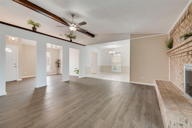 unfurnished living room featuring vaulted ceiling with beams, a fireplace, dark wood-type flooring, baseboards, and ceiling fan with notable chandelier