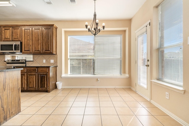 kitchen featuring light tile patterned floors, appliances with stainless steel finishes, backsplash, hanging light fixtures, and a chandelier