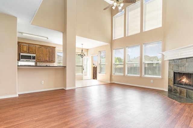 unfurnished living room with a high ceiling, a tile fireplace, wood-type flooring, and ceiling fan with notable chandelier