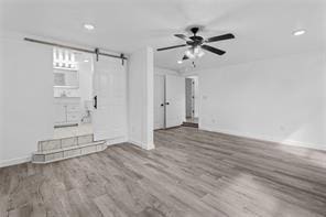 unfurnished living room featuring ceiling fan, wood-type flooring, and a barn door