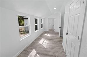 hall featuring vaulted ceiling, built in features, and light hardwood / wood-style flooring