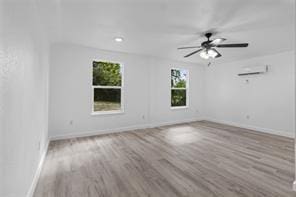 spare room with ceiling fan, a wall unit AC, and light hardwood / wood-style floors