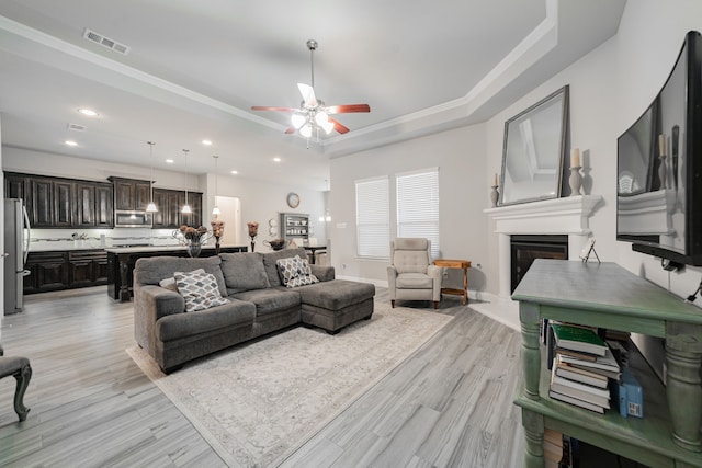 living room with crown molding, ceiling fan, a raised ceiling, and light hardwood / wood-style floors