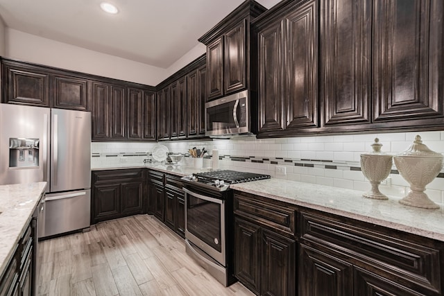 kitchen featuring stainless steel appliances, light stone countertops, backsplash, and dark brown cabinetry