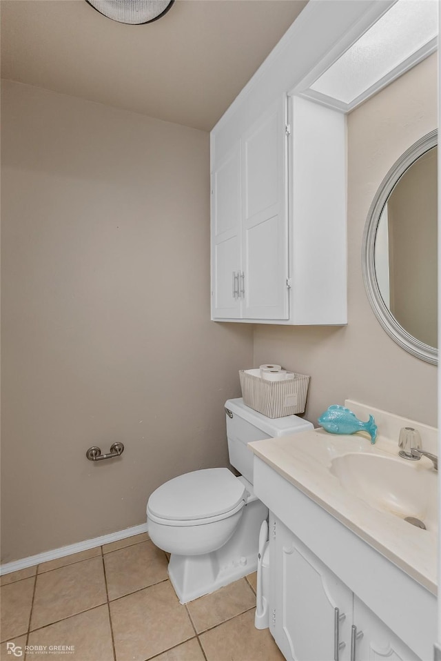 half bath with tile patterned flooring, toilet, a skylight, vanity, and baseboards