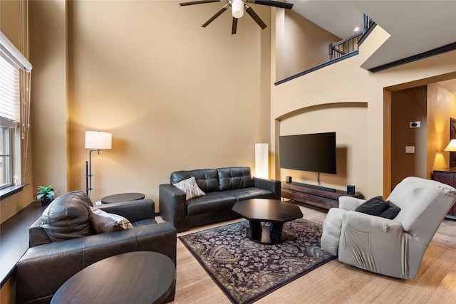 living room with a high ceiling, ceiling fan, and light wood-type flooring