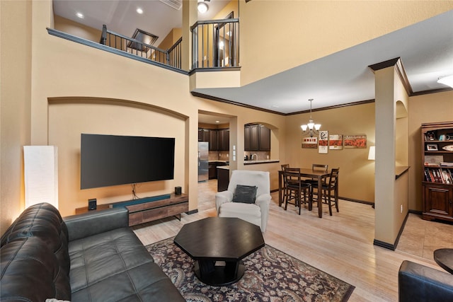 living room featuring a high ceiling, ornamental molding, a chandelier, and light hardwood / wood-style floors