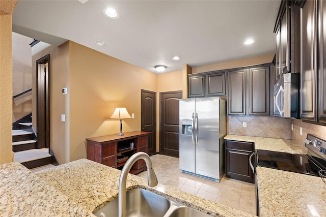 kitchen featuring appliances with stainless steel finishes, tasteful backsplash, light tile patterned floors, dark brown cabinetry, and light stone countertops