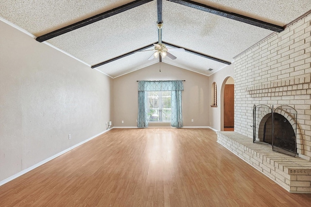 unfurnished living room featuring ceiling fan, vaulted ceiling with beams, wood-type flooring, a textured ceiling, and a brick fireplace