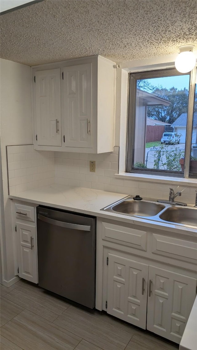 kitchen featuring sink, backsplash, white cabinets, a textured ceiling, and stainless steel dishwasher