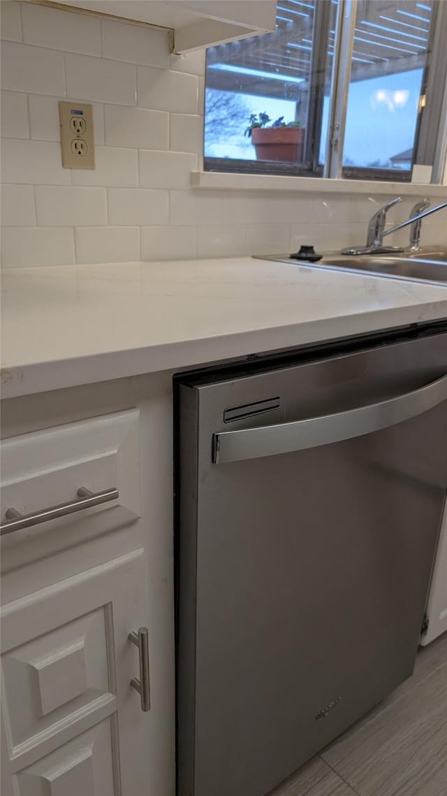 details featuring white cabinetry, stainless steel dishwasher, sink, and backsplash