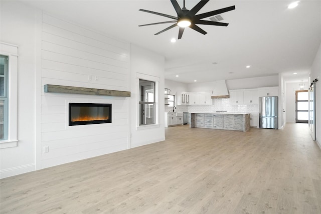 unfurnished living room featuring sink, a fireplace, light hardwood / wood-style floors, and ceiling fan