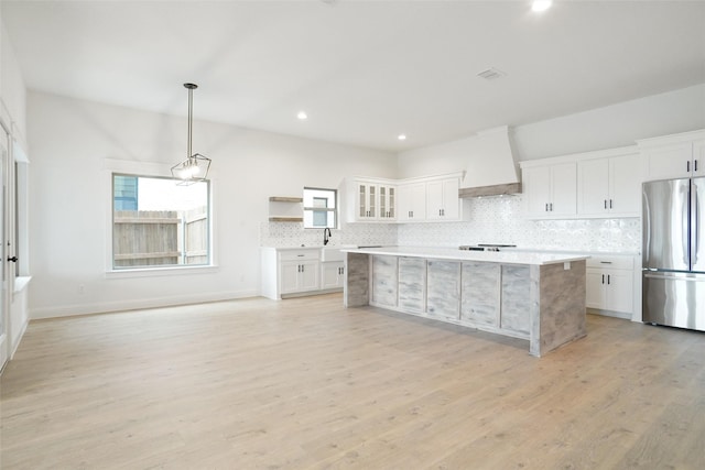 kitchen with stainless steel fridge, hanging light fixtures, white cabinets, decorative backsplash, and custom exhaust hood