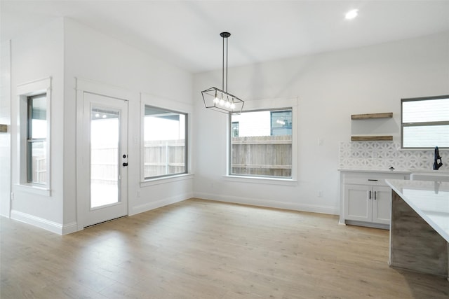 unfurnished dining area featuring a notable chandelier, sink, and light wood-type flooring