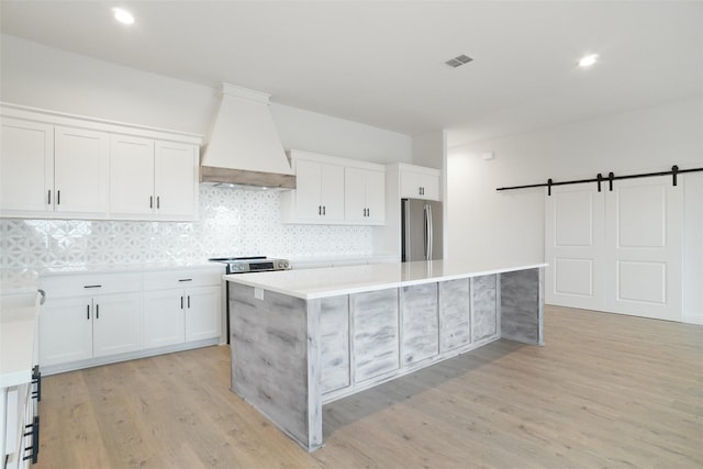 kitchen with a center island, custom range hood, stainless steel appliances, a barn door, and white cabinets