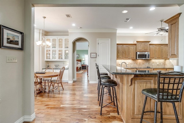 kitchen with arched walkways, stainless steel microwave, a breakfast bar, and light wood-style flooring