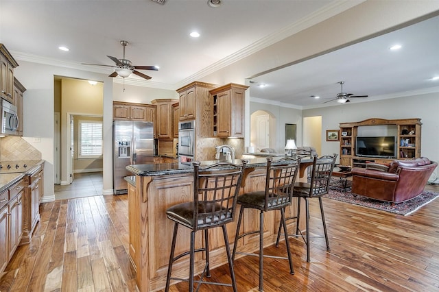 kitchen featuring a breakfast bar area, a ceiling fan, appliances with stainless steel finishes, and light wood-style floors