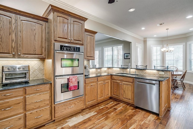kitchen featuring appliances with stainless steel finishes, tasteful backsplash, a sink, a peninsula, and hardwood / wood-style floors