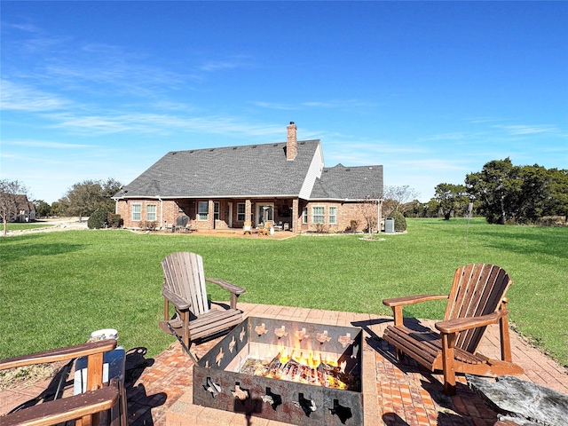rear view of property featuring a yard, brick siding, a chimney, and an outdoor fire pit