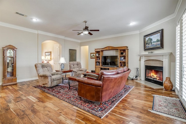 living room featuring a ceiling fan, visible vents, arched walkways, wood finished floors, and ornamental molding