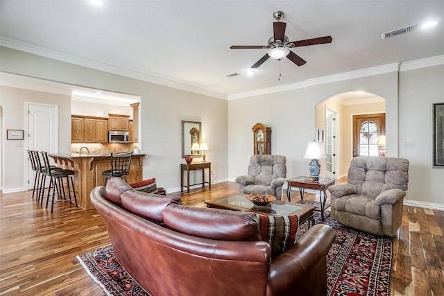 living room featuring visible vents, a ceiling fan, crown molding, wood finished floors, and arched walkways