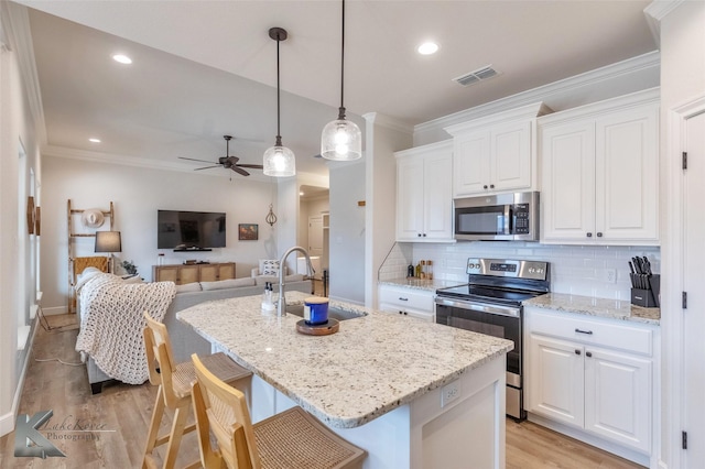 kitchen featuring appliances with stainless steel finishes, sink, light stone counters, white cabinets, and a kitchen island with sink