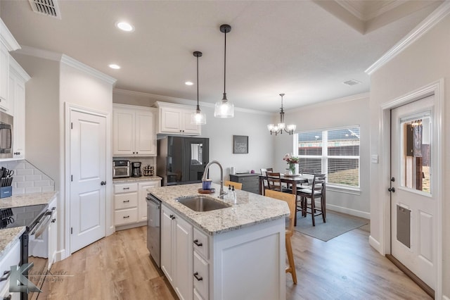 kitchen featuring a center island with sink, sink, light stone counters, decorative light fixtures, and white cabinets