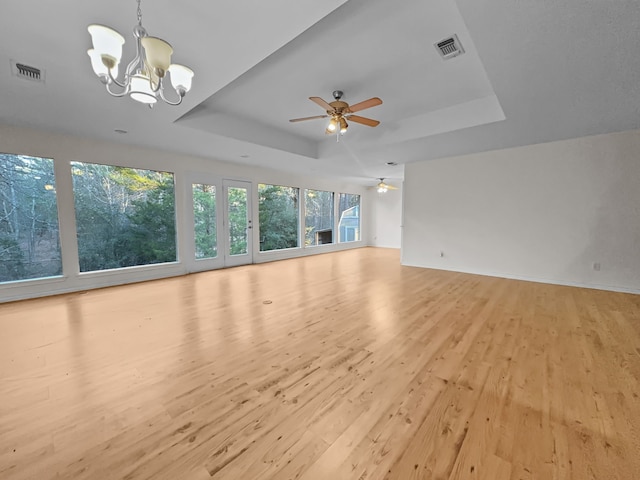 unfurnished living room featuring ceiling fan with notable chandelier, light wood-type flooring, and a raised ceiling