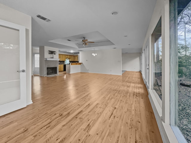 1476 W Holly Trl, Holly Lake Ranch, TX 75765 - unfurnished living room featuring light wood-style flooring, visible vents, ceiling fan, a tray ceiling, and a fireplace