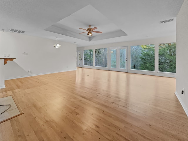 unfurnished living room featuring a raised ceiling, light hardwood / wood-style flooring, and ceiling fan with notable chandelier