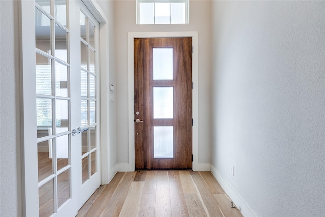 entrance foyer with baseboards, french doors, and light wood-style floors