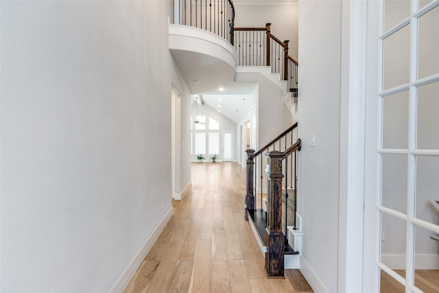 hall with light wood-style flooring, a towering ceiling, baseboards, and stairs