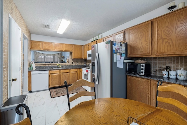 kitchen featuring tasteful backsplash, sink, dark stone countertops, white appliances, and a textured ceiling