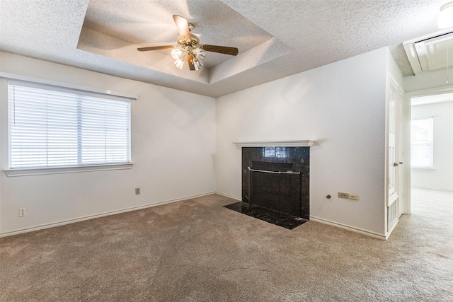 unfurnished living room featuring carpet, attic access, a ceiling fan, a high end fireplace, and a tray ceiling