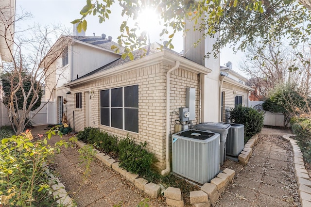 view of property exterior with brick siding, central AC, and fence