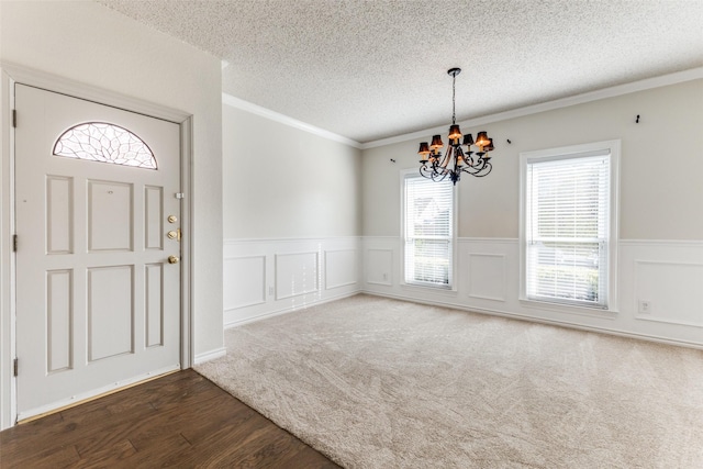 entryway with crown molding, dark wood-style floors, a textured ceiling, a wainscoted wall, and a notable chandelier