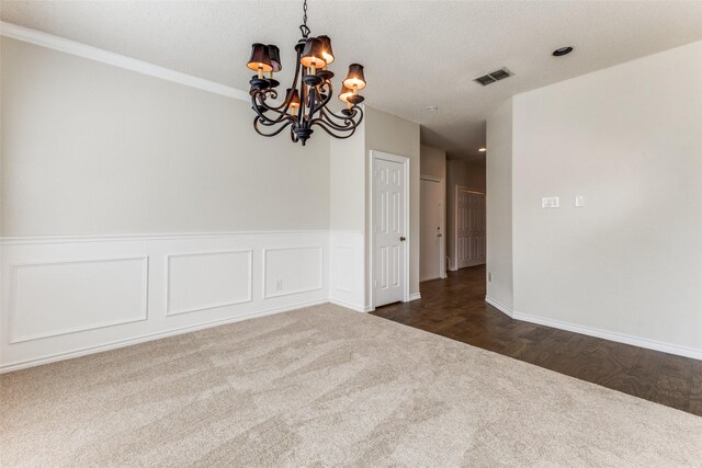 spare room featuring dark carpet, wainscoting, visible vents, and an inviting chandelier