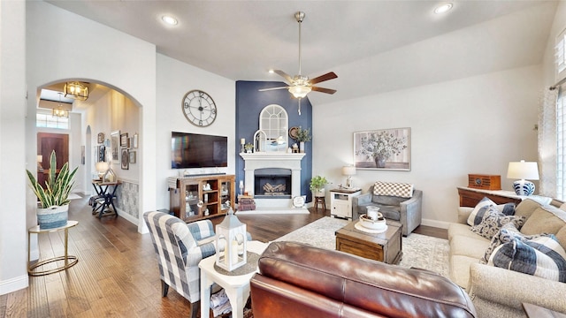 living room featuring baseboards, arched walkways, wood finished floors, and a glass covered fireplace