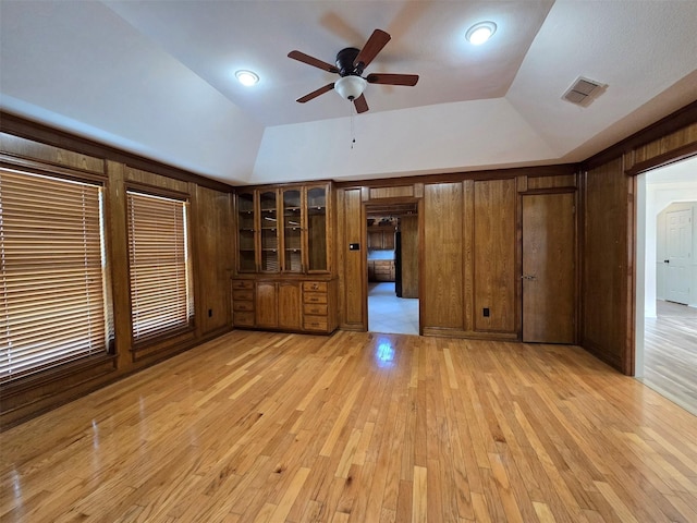 unfurnished living room featuring wooden walls, light wood-type flooring, visible vents, and lofted ceiling