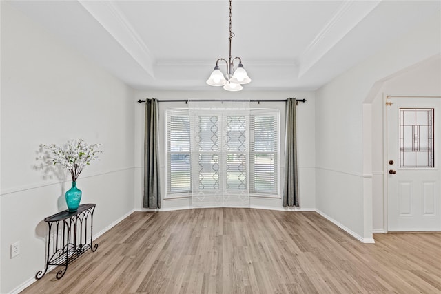 unfurnished dining area with light wood finished floors, a raised ceiling, and crown molding