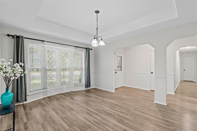 interior space with arched walkways, baseboards, light wood-style flooring, a tray ceiling, and crown molding