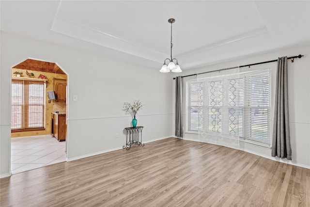 unfurnished dining area with arched walkways, a raised ceiling, light wood finished floors, and an inviting chandelier