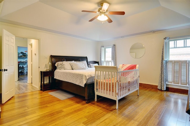 bedroom with a tray ceiling, a ceiling fan, light wood-style flooring, and baseboards