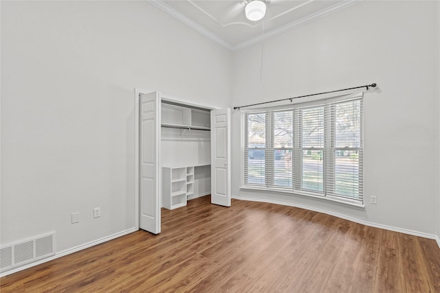 unfurnished bedroom featuring a closet, visible vents, ornamental molding, wood finished floors, and baseboards