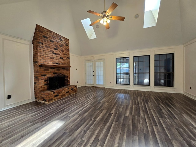 unfurnished living room with a decorative wall, a skylight, a ceiling fan, a brick fireplace, and dark wood finished floors