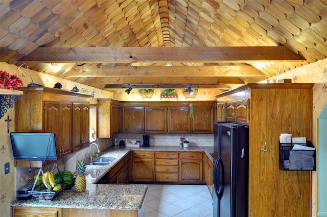 kitchen with light stone counters, beamed ceiling, freestanding refrigerator, a sink, and backsplash