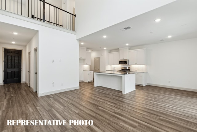 kitchen featuring a kitchen island with sink, hardwood / wood-style floors, stainless steel appliances, tasteful backsplash, and white cabinets